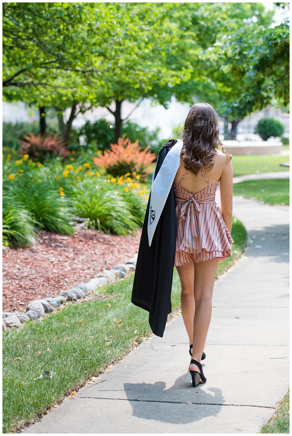 Fenwick High school senior girl walking down a path holding her graduation robes.