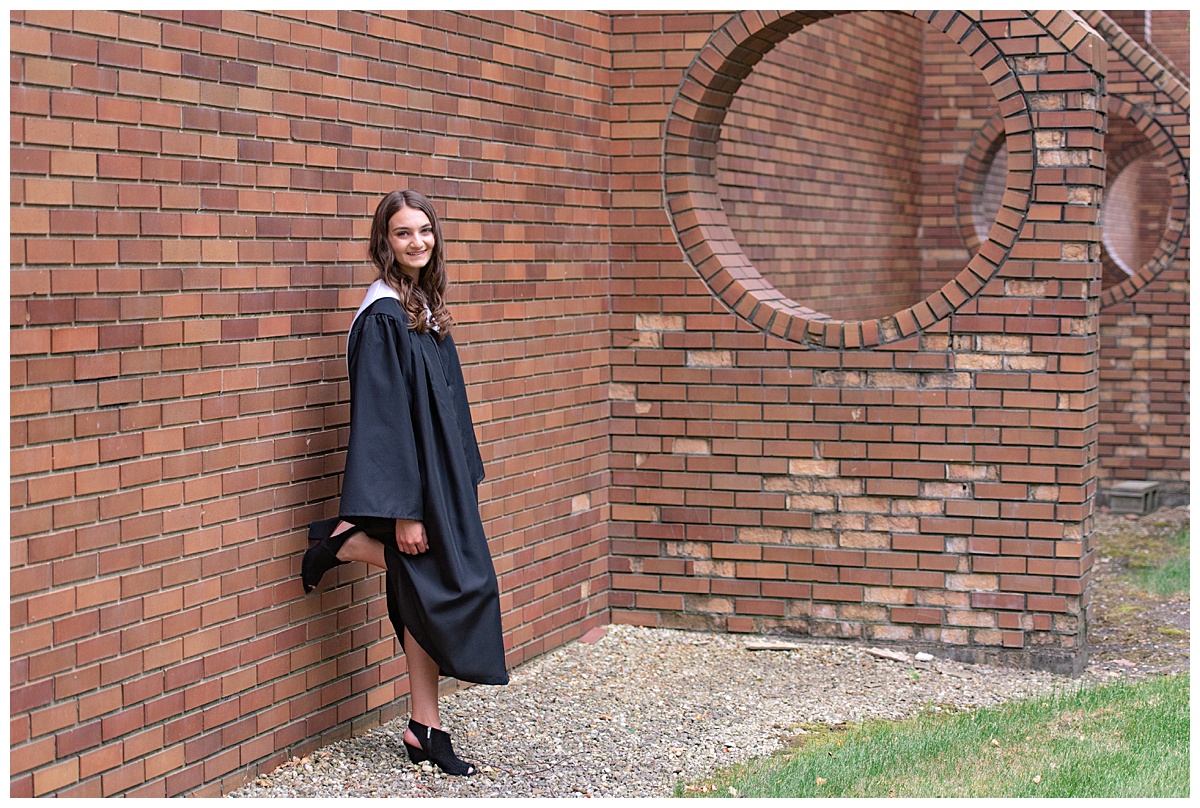 Chicago high school senior girl in graduation robes leaning against a brick wall by Chicago senior photographer Kristen Hazelton