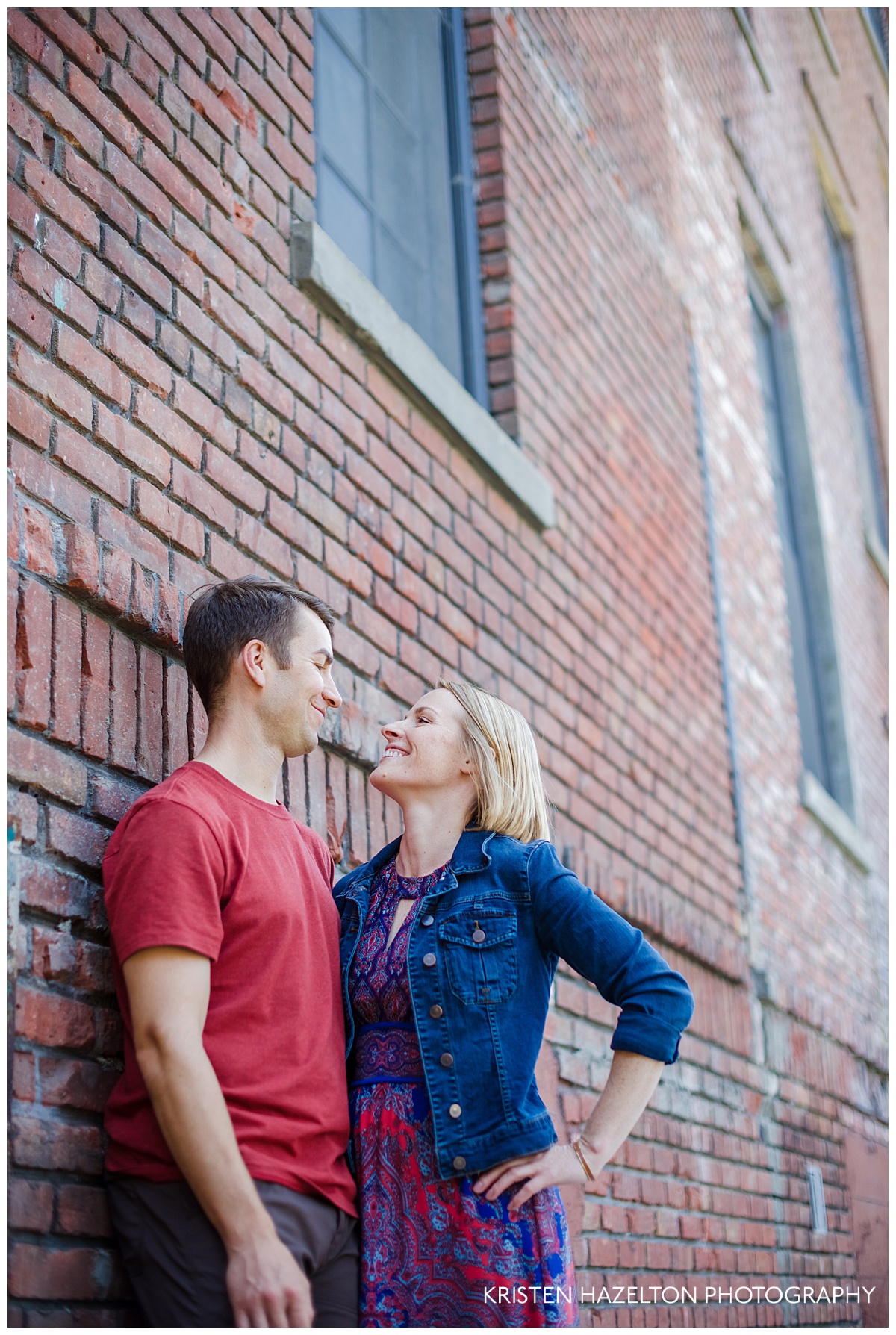 Engaged couple posing next to an old brick building