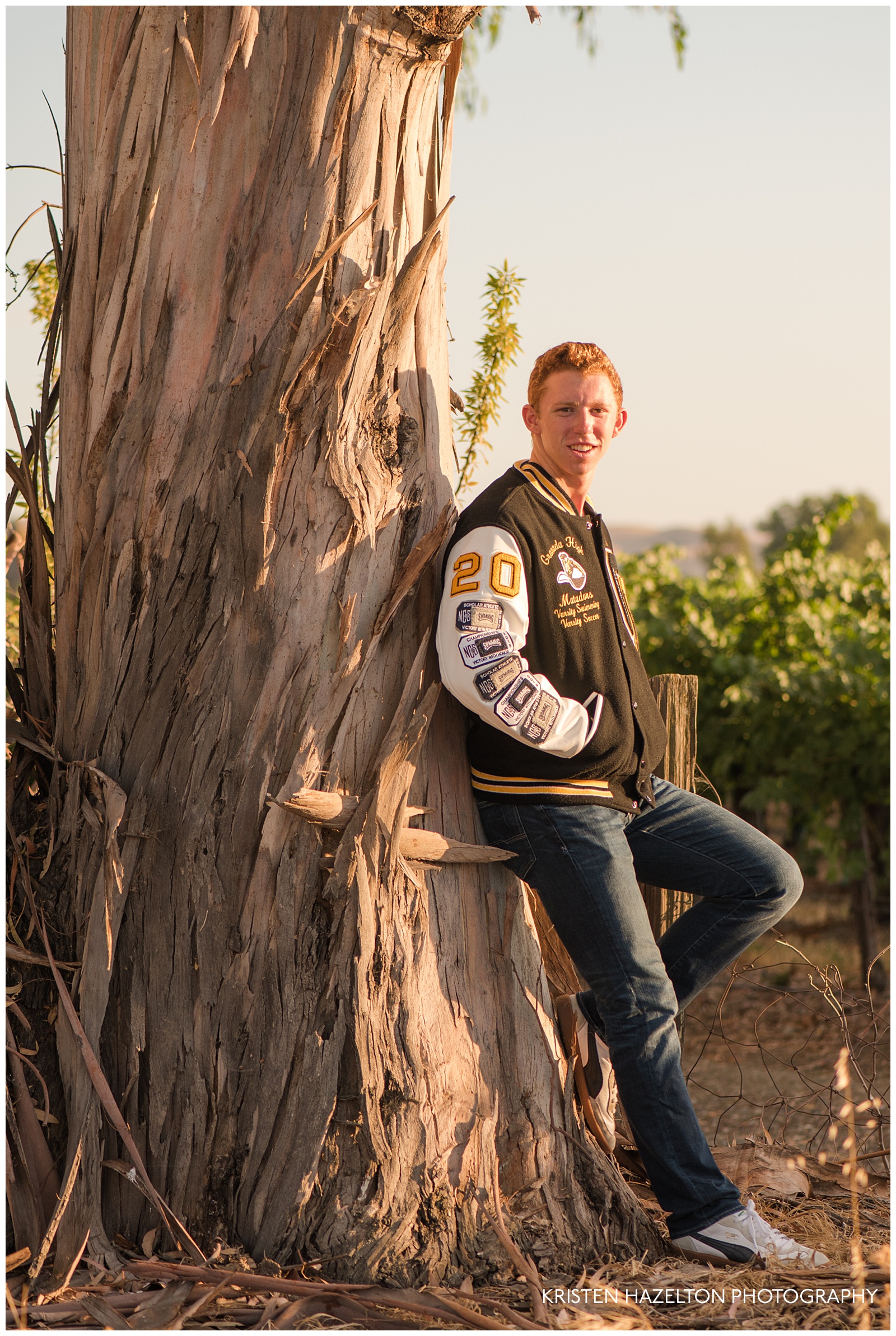 Livermore senior photos of a teen wearing a varsity jacket leaning against a tree