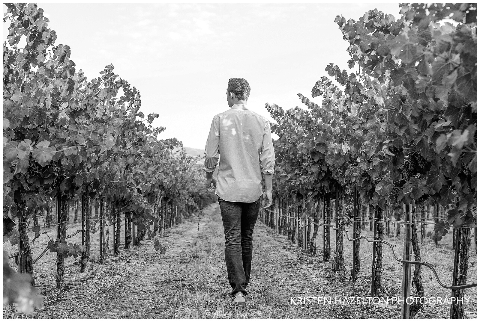 Black and white Livermore senior photos of a teen walking away through grape vines
