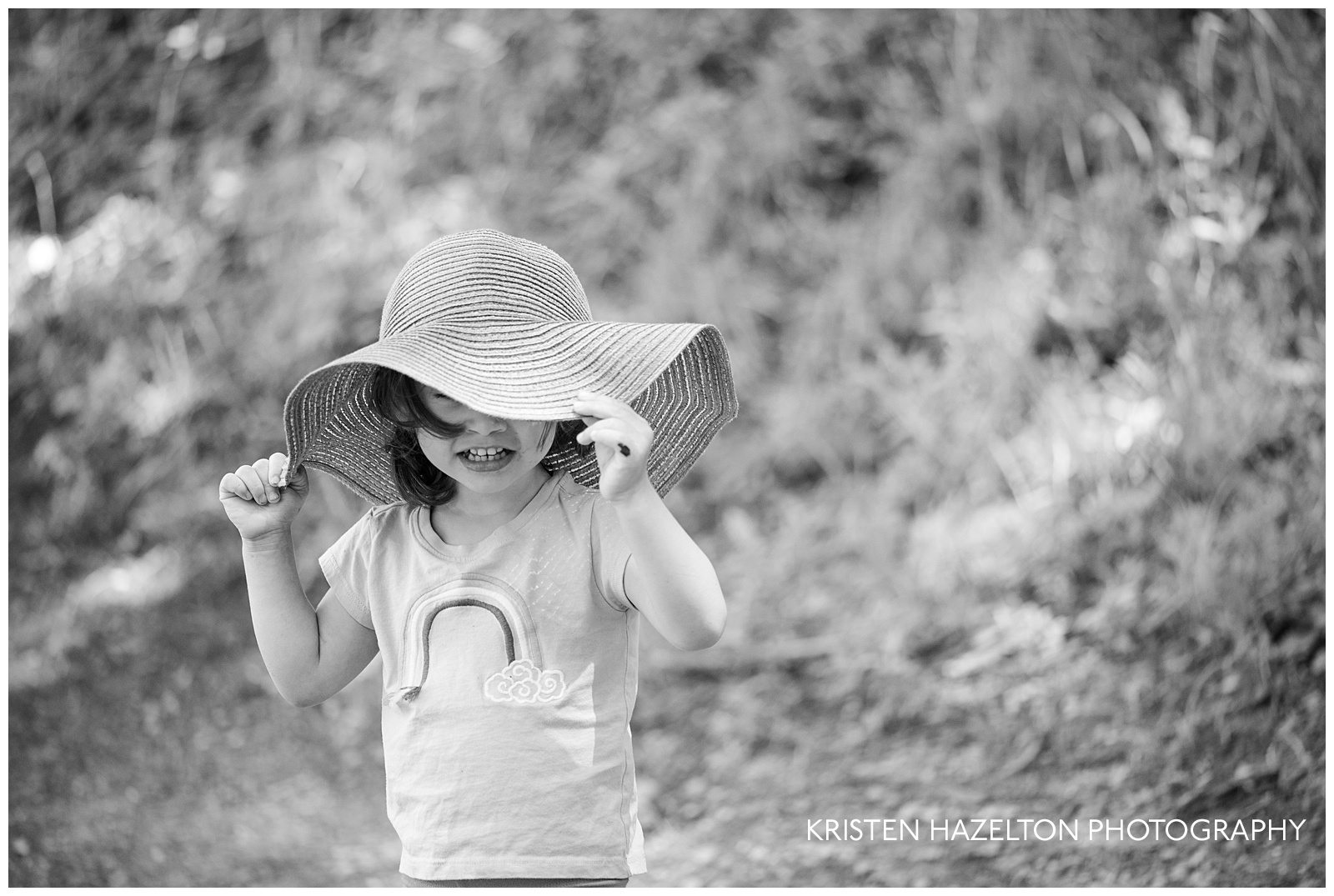 Toddler girl hiding under an adult's wide-brimmed sun hat