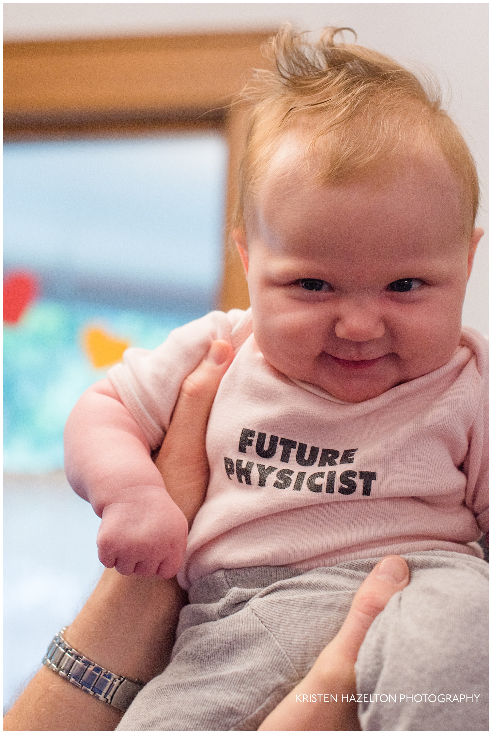Smiling three-month old baby wearing onesie that says "Future Physicist"