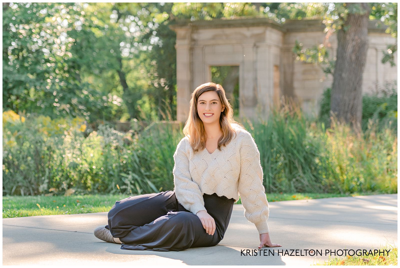UIC graduation portraits - a woman wearing a white crop top sweater and black harem pants sitting on a path