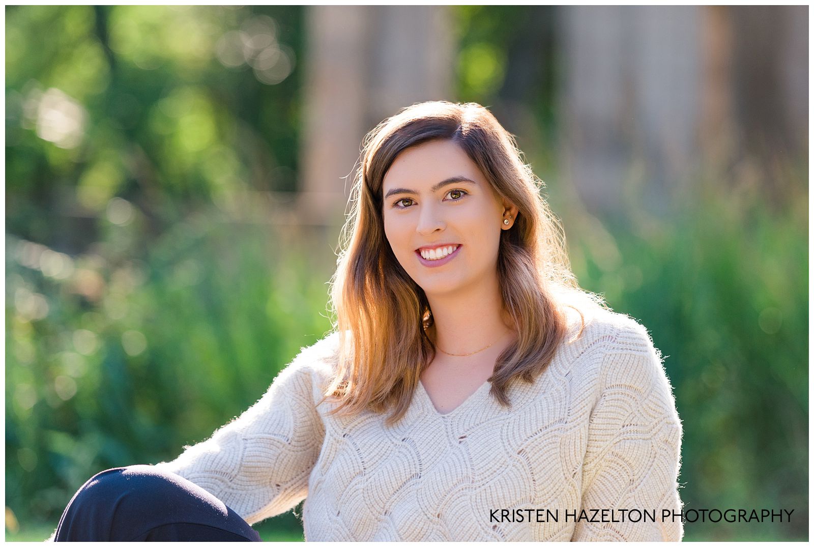 UIC graduation portraits: a woman in a white sweater crop top and black harem pants in a sunny park