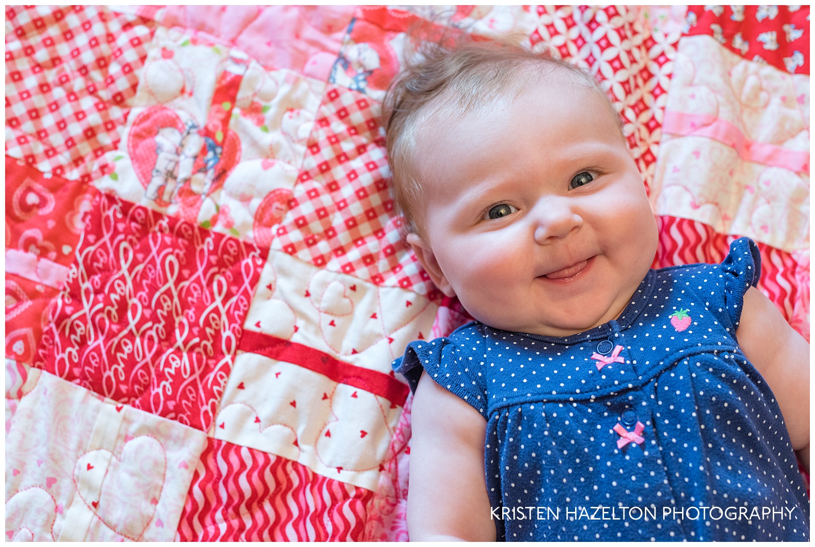 four month old smiling up from a red quilt