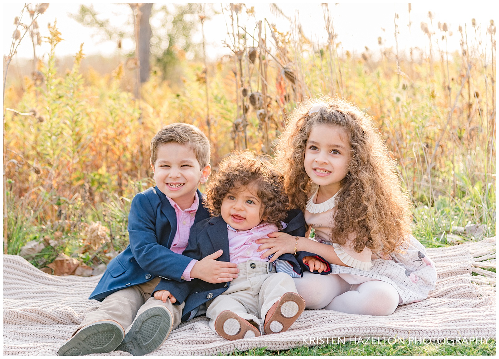 Three young siblings smiling in a meadow