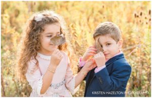 A brother and a sister playing peekaboo behind fall leaves