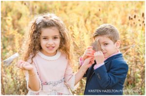 A brother and a sister playing peekaboo behind fall leaves
