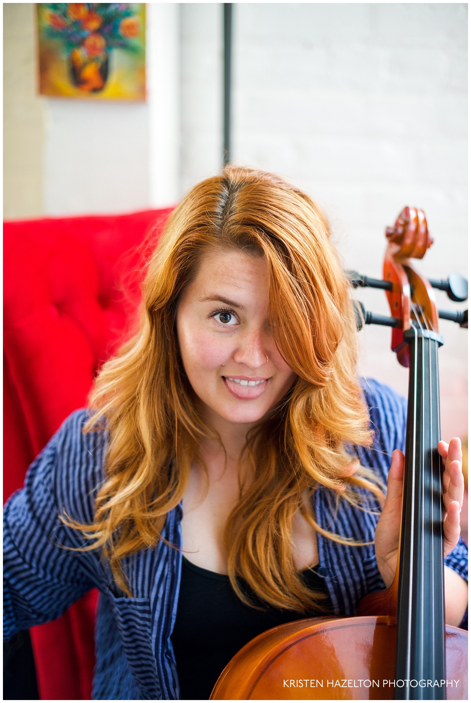 portrait of a redheaded woman playing a cello while sticking out her tongue