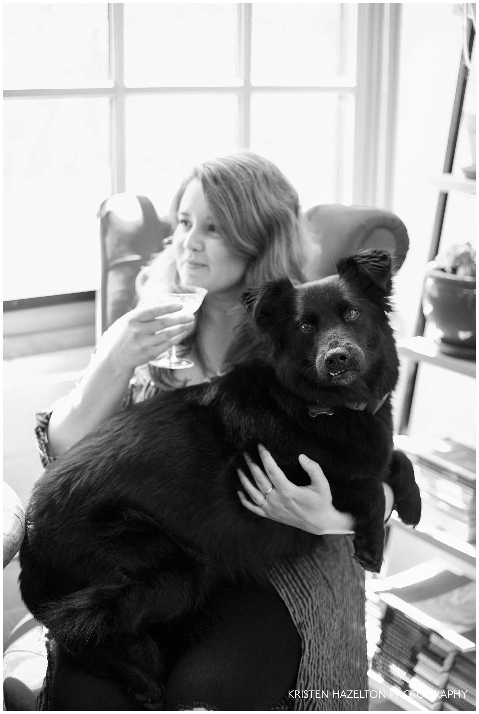 black and white portrait of a woman drinking champagne and holding a large black dog on her lap