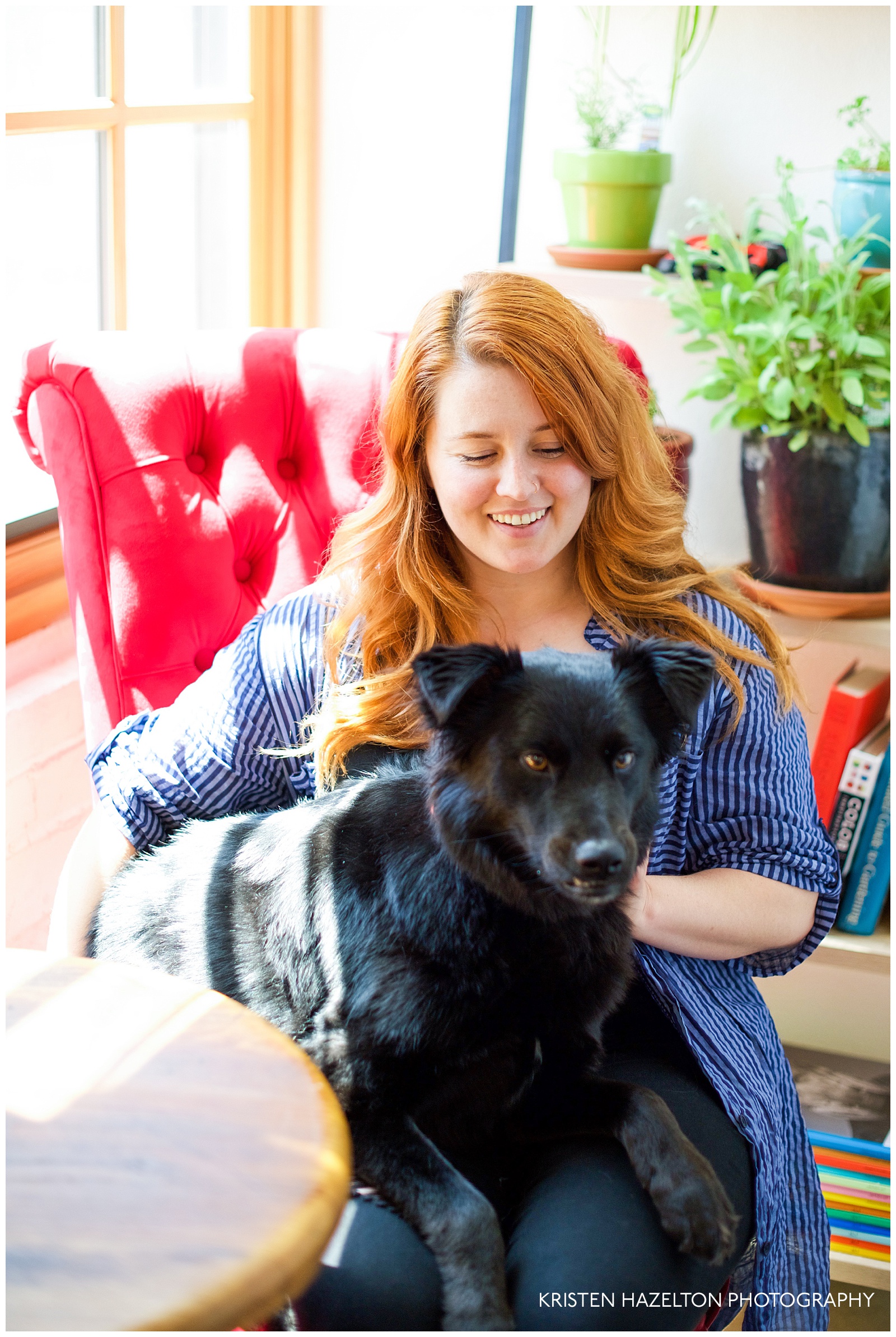 redheaded woman on a red chair holding a snaggletoothed black dog