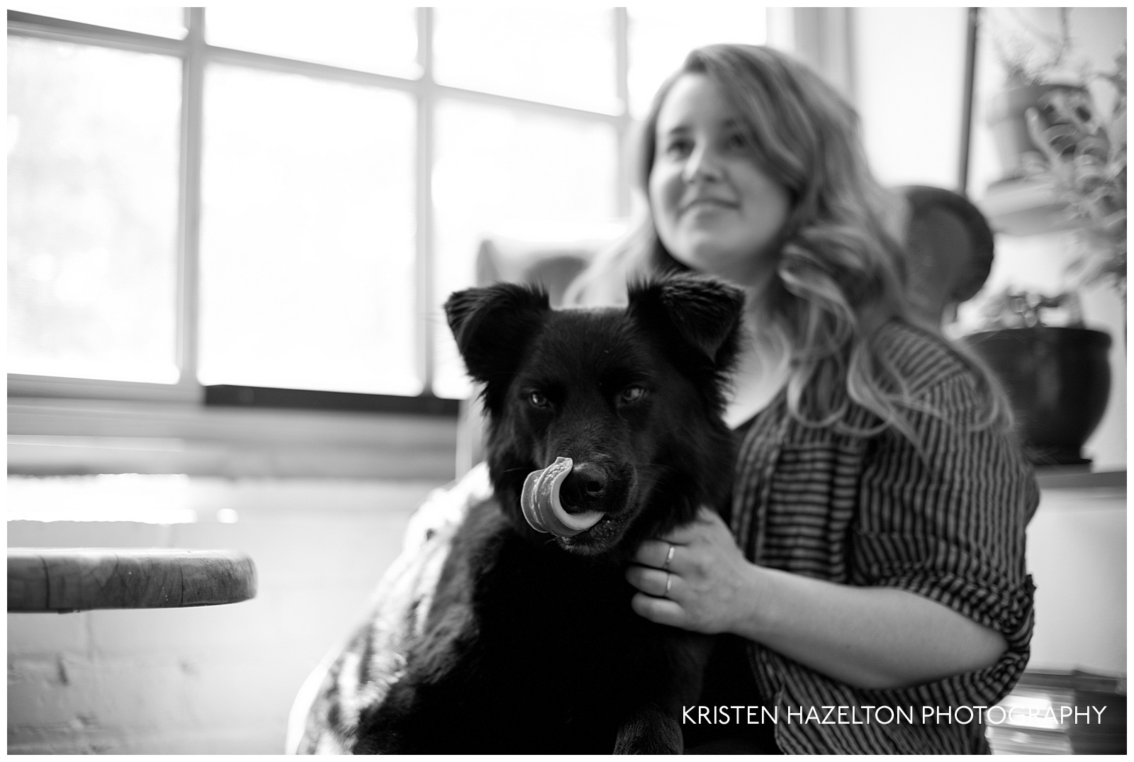 black and white portrait of a woman holding her large black dog who is licking a booger