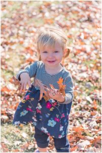 A toddler proudly showing off a pile of leaves