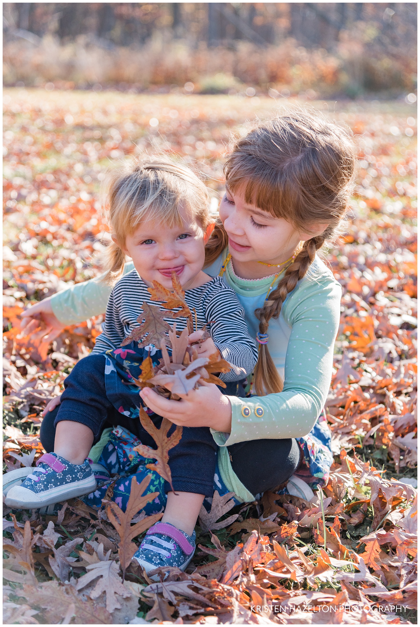 Fall family portraits of Two sisters sitting and throwing leaves together