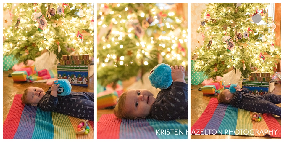 Happy baby on a rainbow blanket under a christmas tree chewing on a blue soft ornament