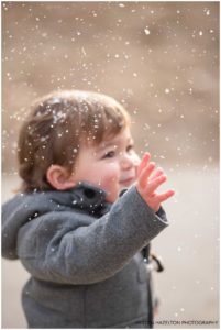 Toddler reaching up to touch falling snowflakes