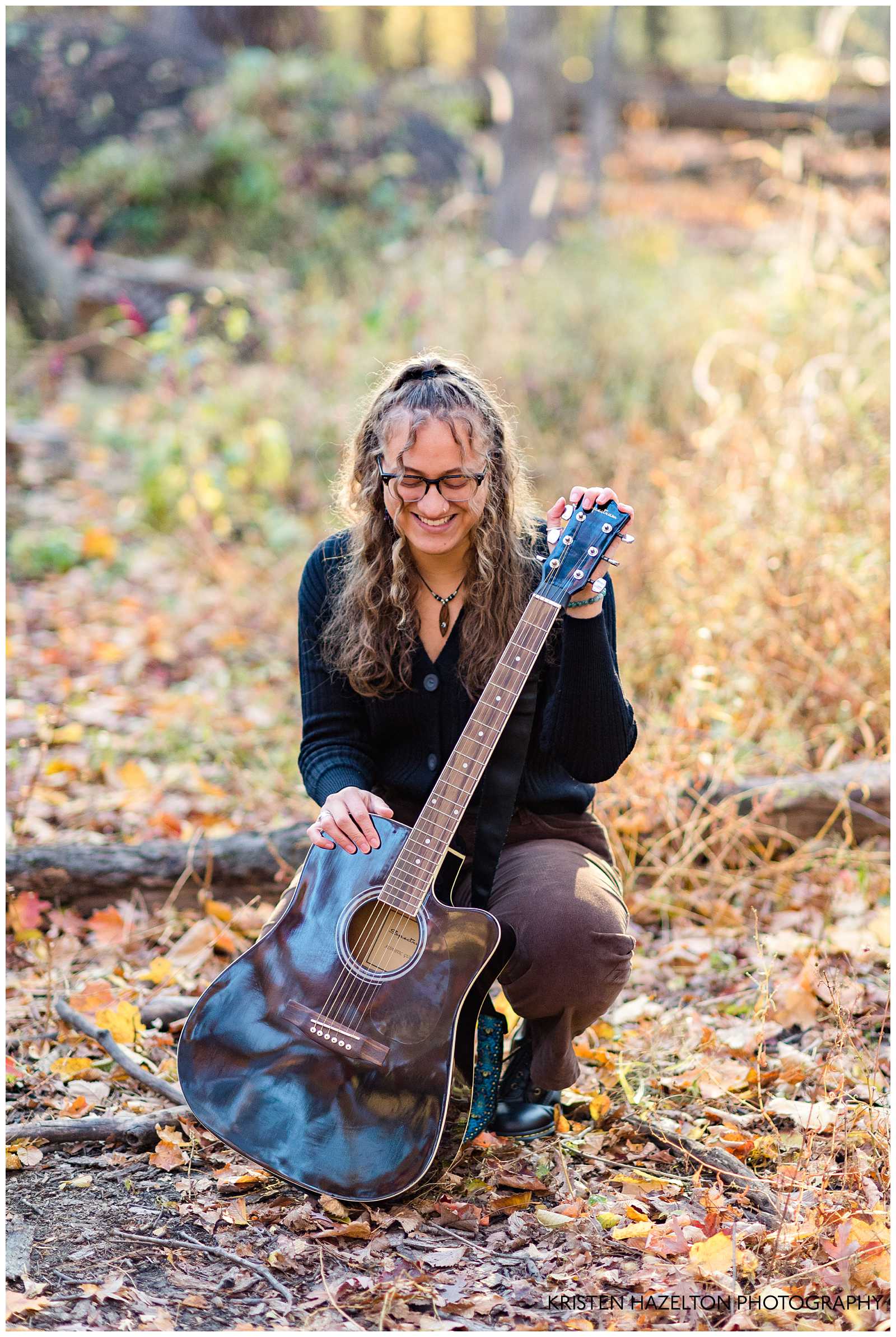 Senior portrait of a girl crouching with her acoustic guitar in the woods