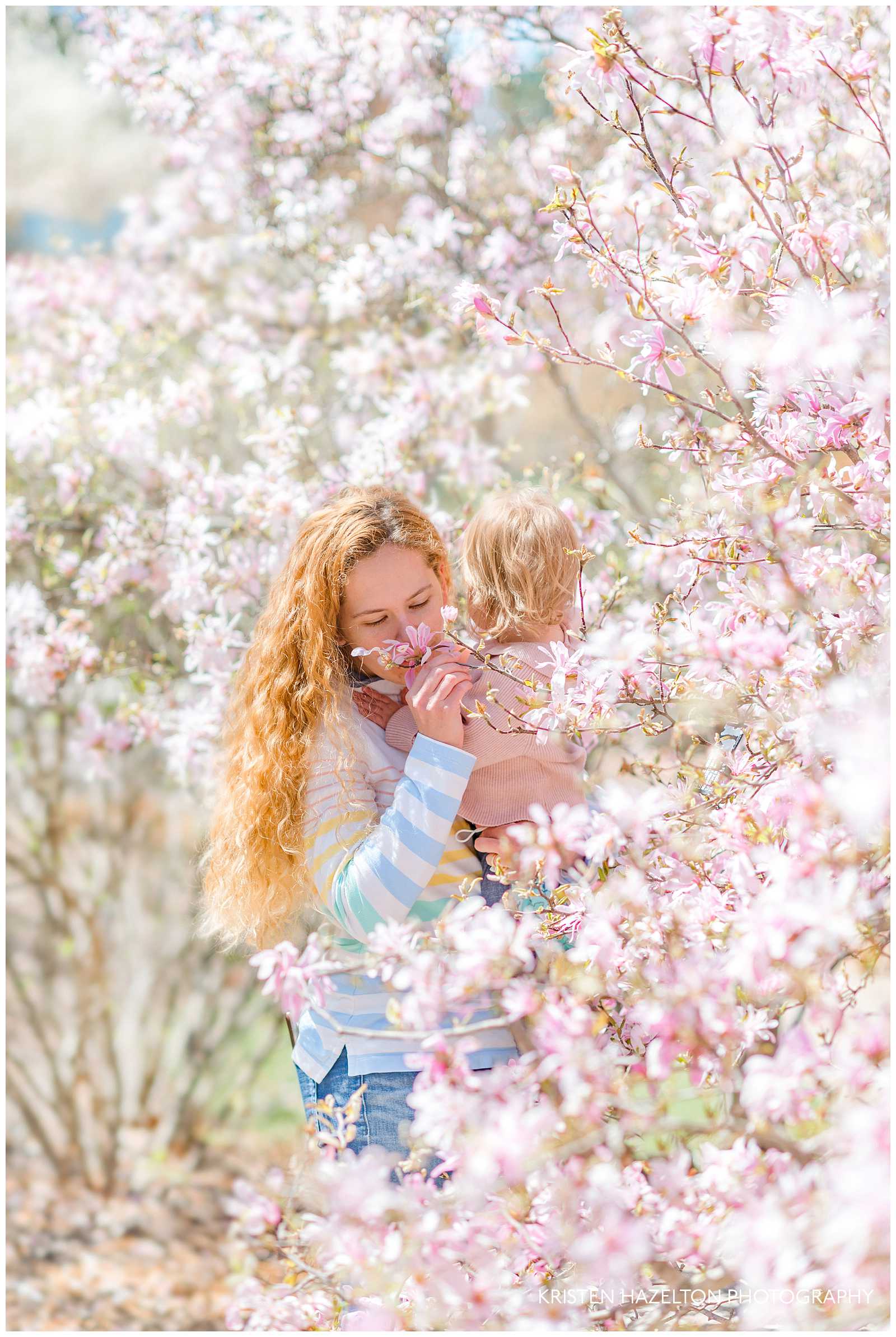 Morton Arboretum photography of a 
 redheaded woman holding her baby and smelling a pink star magnolia.