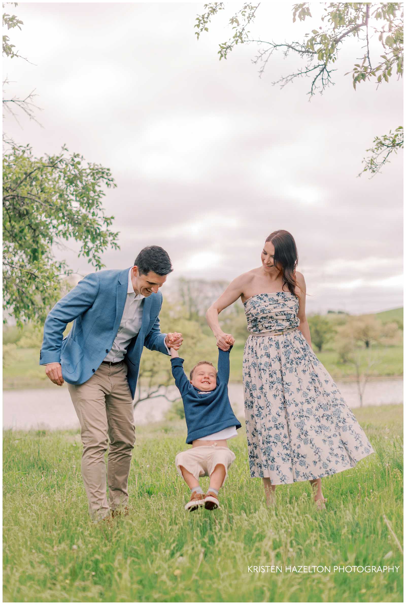 Family of three swinging their toddler boy on a grassy hill for their Morton Arboretum photos