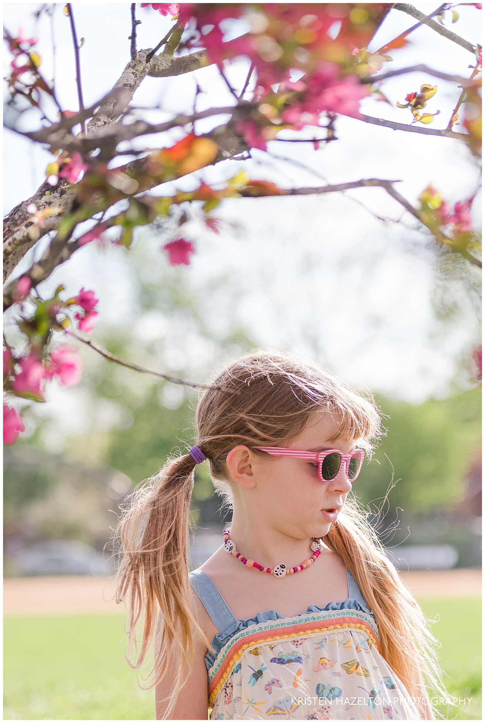 Young girl with pink sunglasses underneath a crabapple tree with pink blossoms