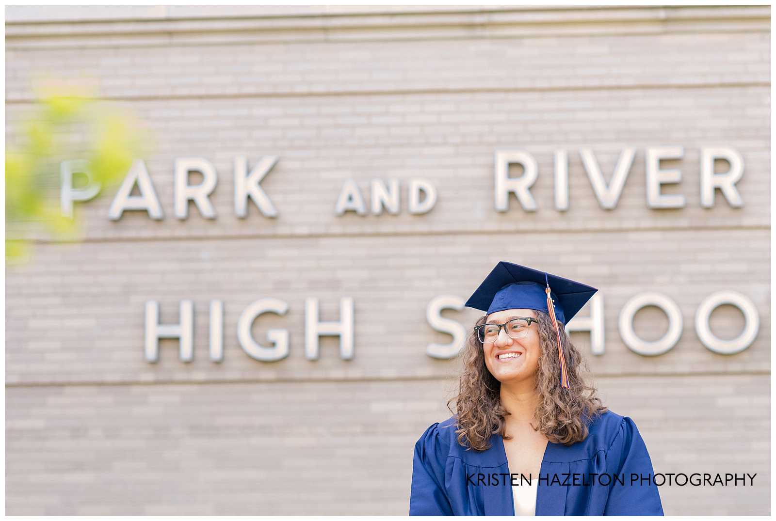 High school senior wearing cap and gown smiling in front of Oak Park River Forest High School