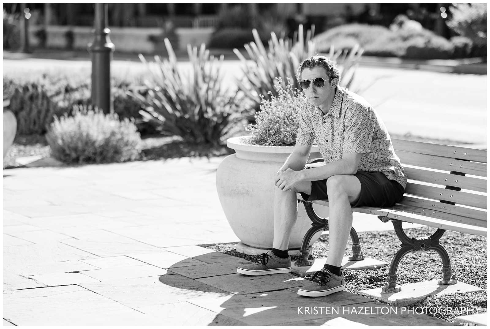 Black and white photo of a male high school senior wearing aviator sunglasses and sitting on a bench in downtown Livermore, CA