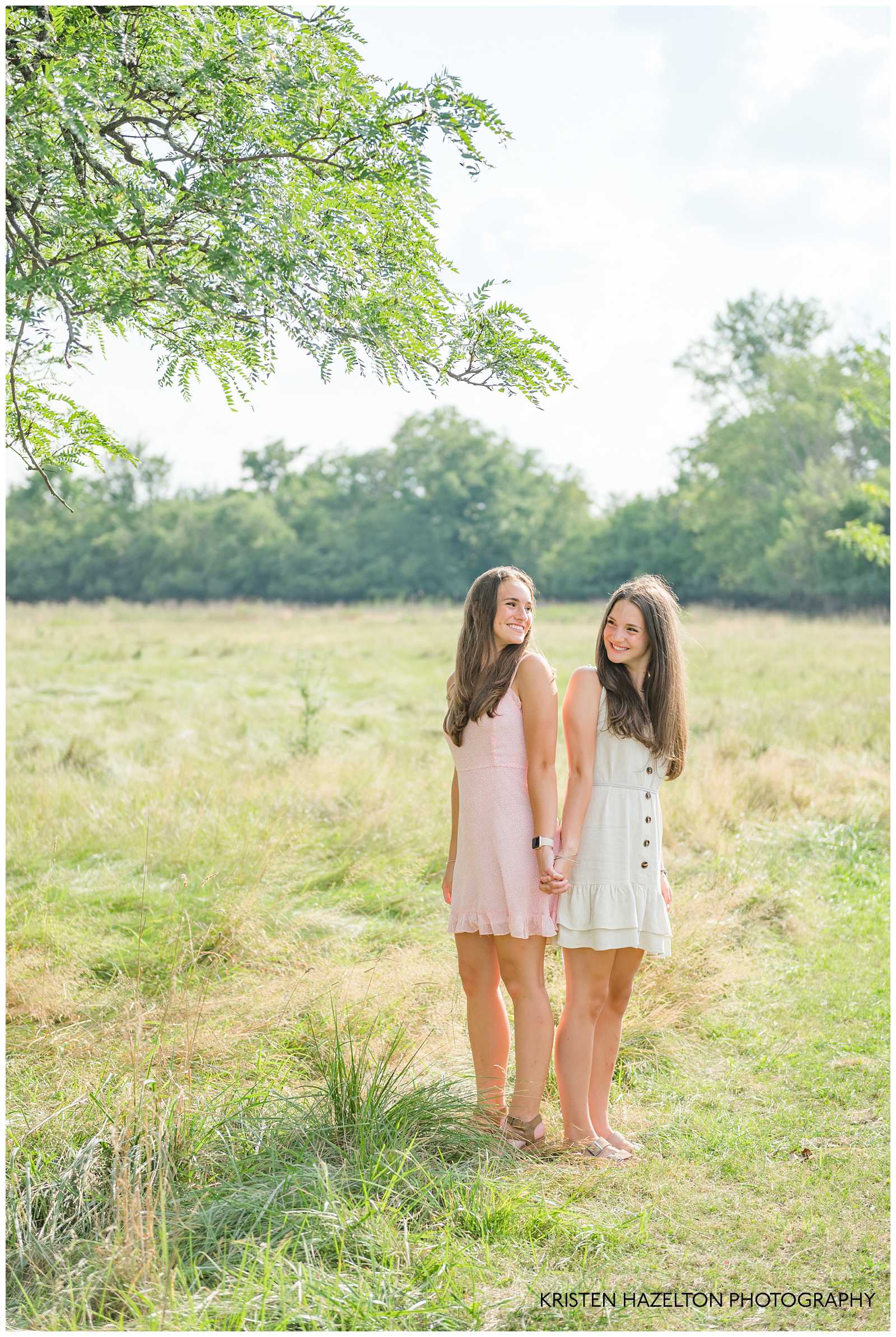 Two teenage sisters back to back, smiling at each other by Elmhurst, IL photographer Kristen Hazelton