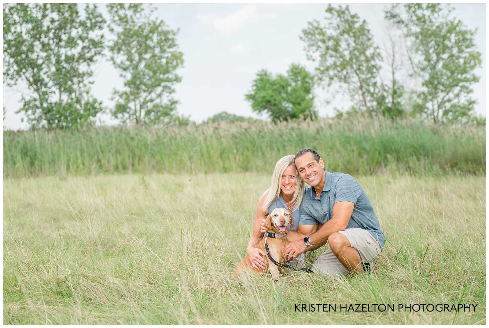 Husband and wife petting their dog in a field