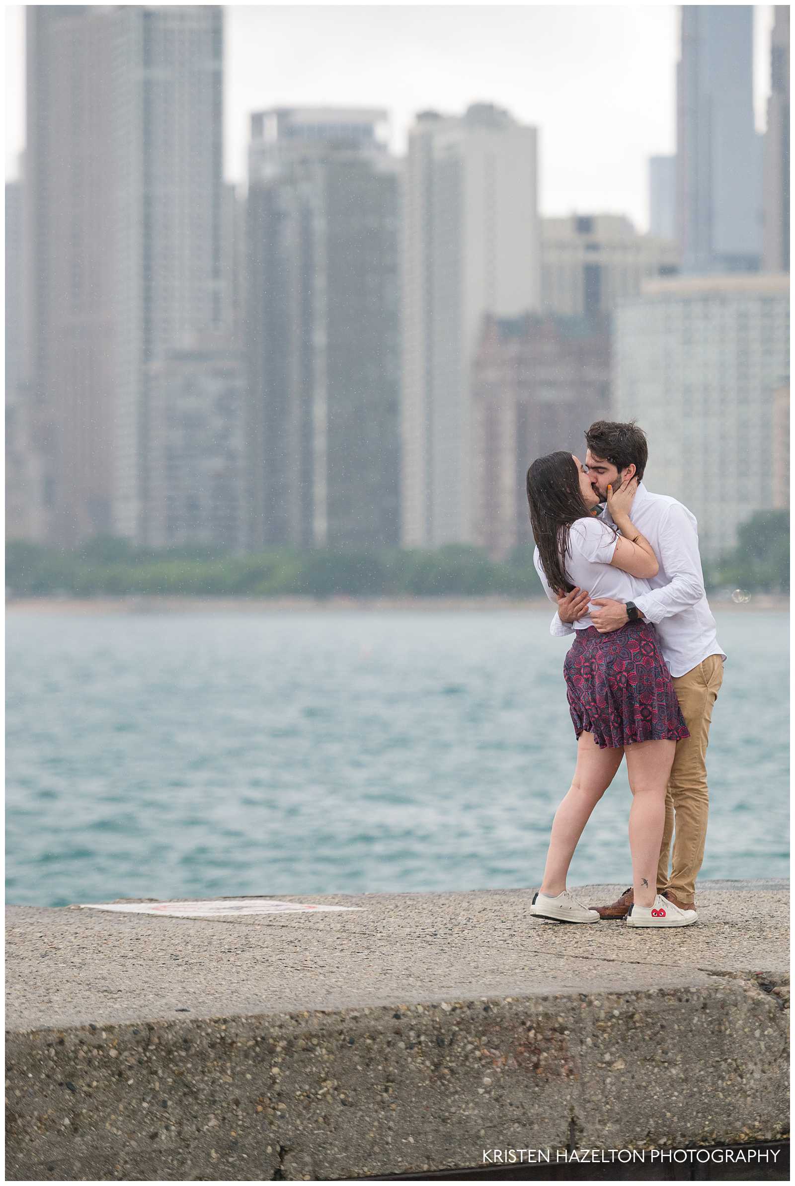 Newly engaged couple kissing in the rain in front of the Chicago skyline