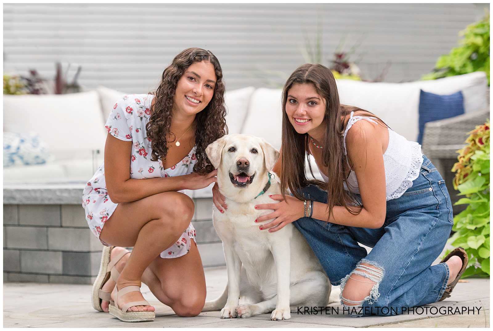 Two adult sisters smiling with their golden labrador in their backyard photoshoot