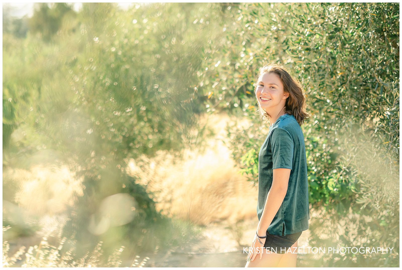 Girl wearing a green shirt and black shorts with golden grass in an olive grove for her Holdener Park Photos