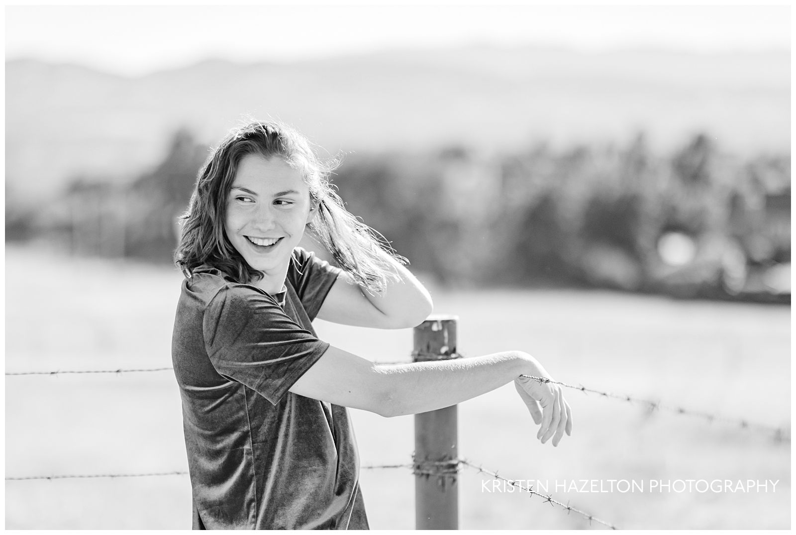 Black and white photo of a girl resting her hand on a barbed wire fence