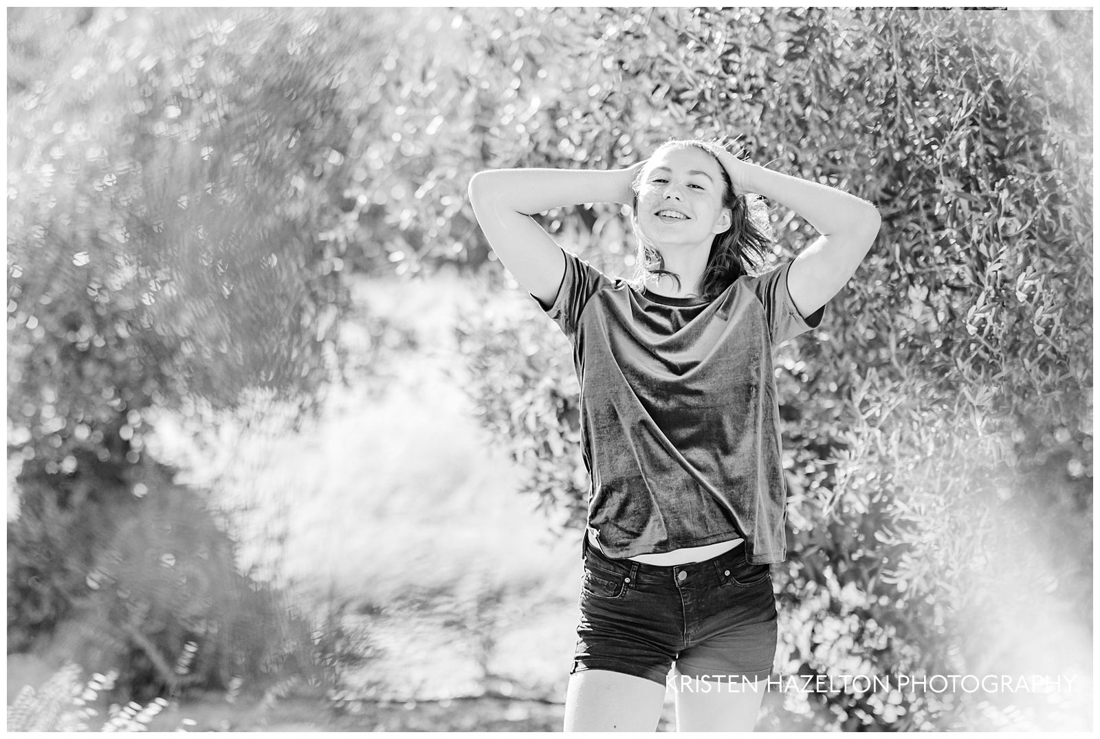 black and white photo of a girl with her hands in her hair in an olive grove
