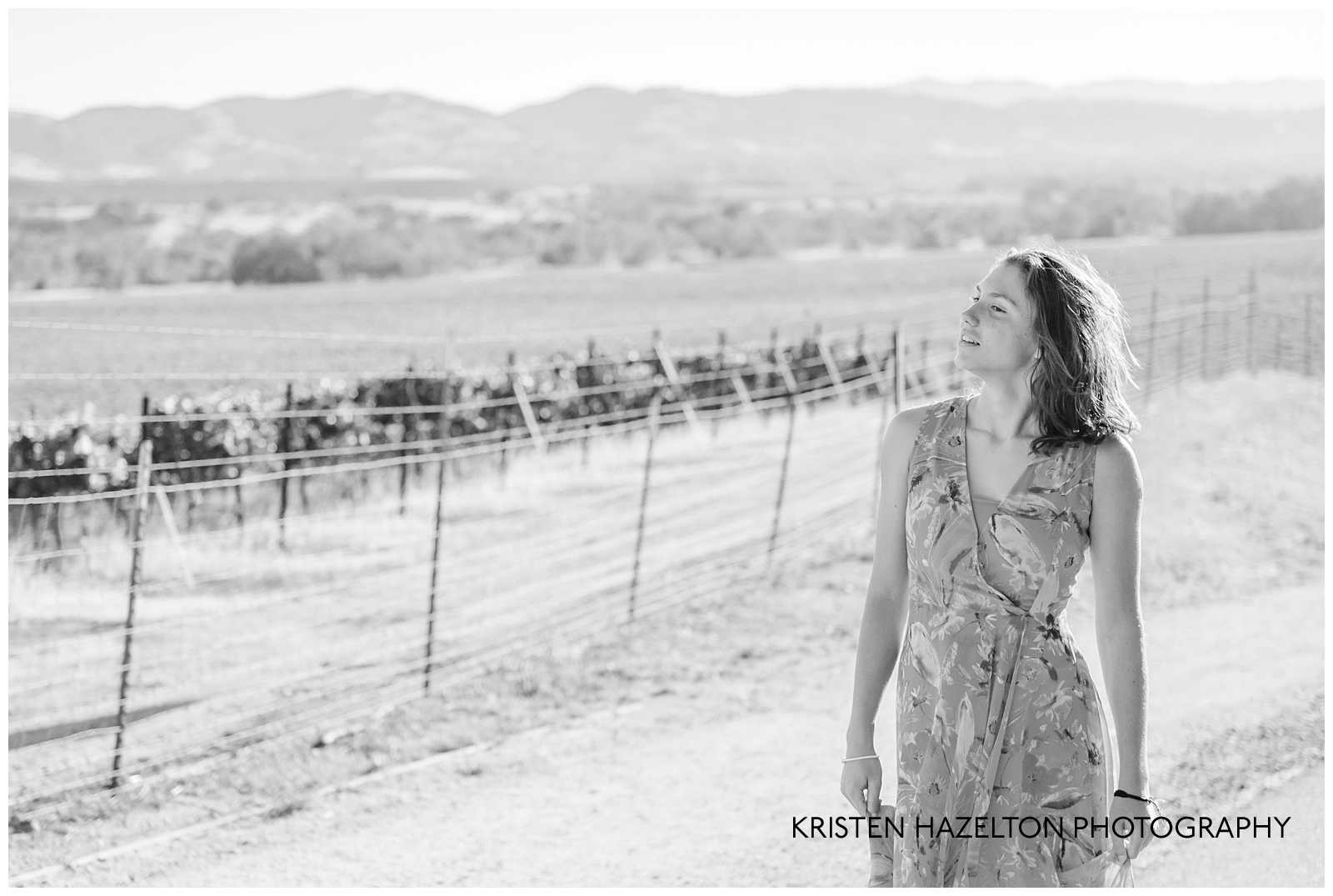 black and white photo of a girl walking next to vineyards