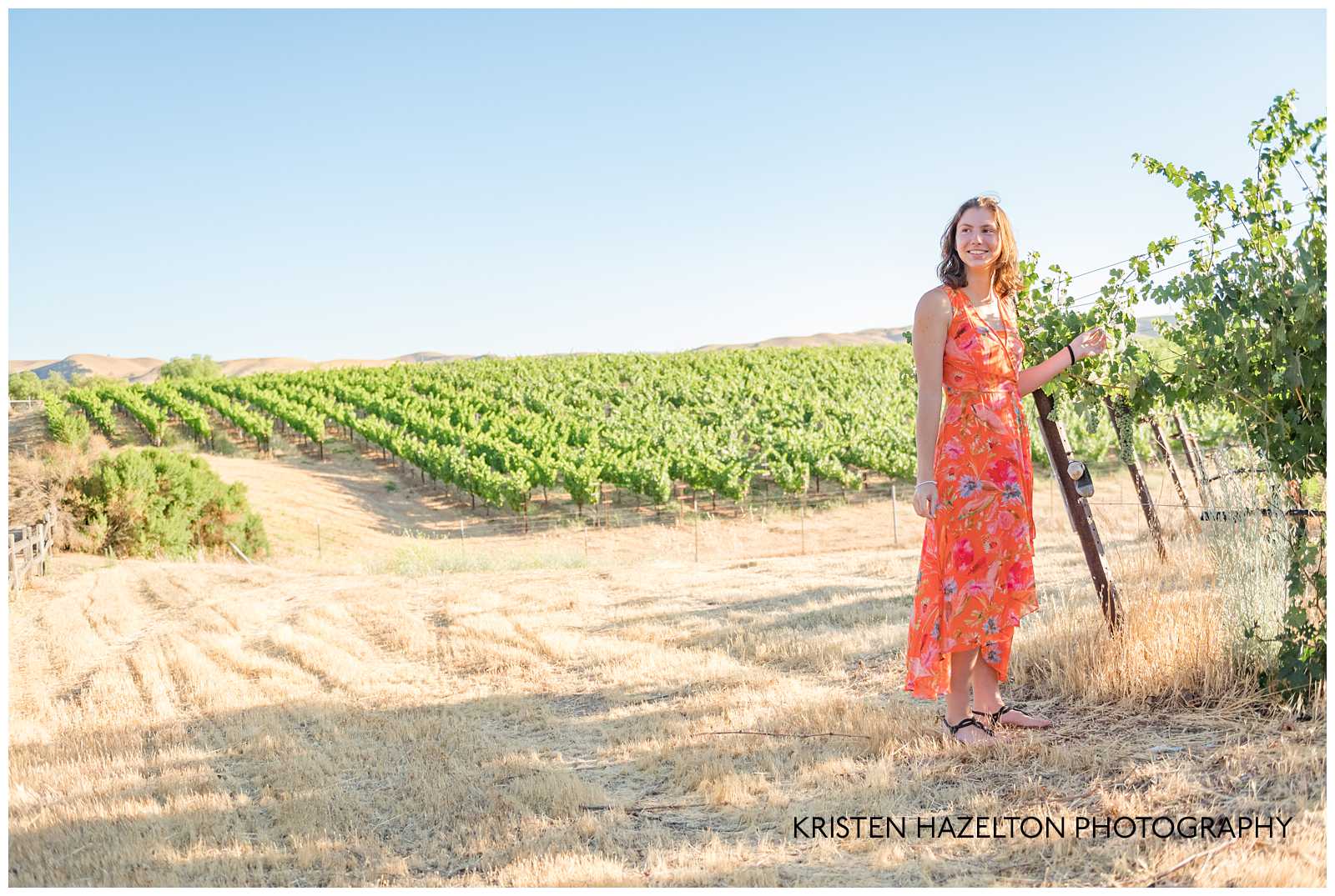 Girl in orange dress standing next to grape vines