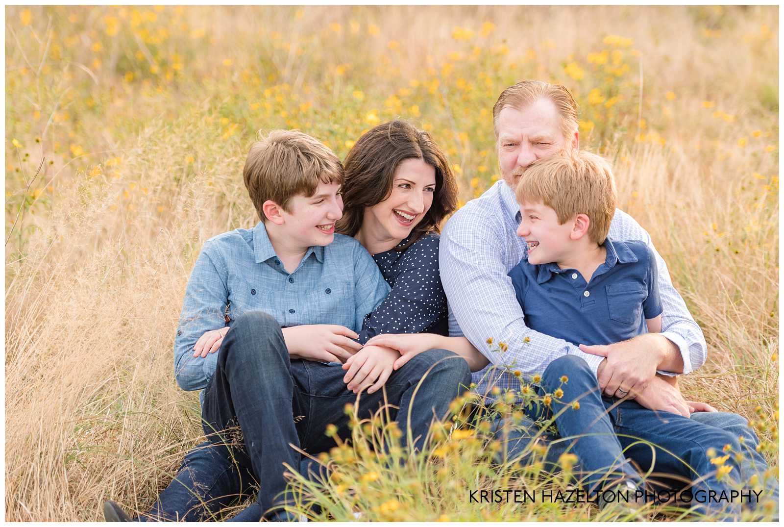 Family of four sitting in a field and laughing at each other by Berwyn, IL photographer Kristen Hazelton