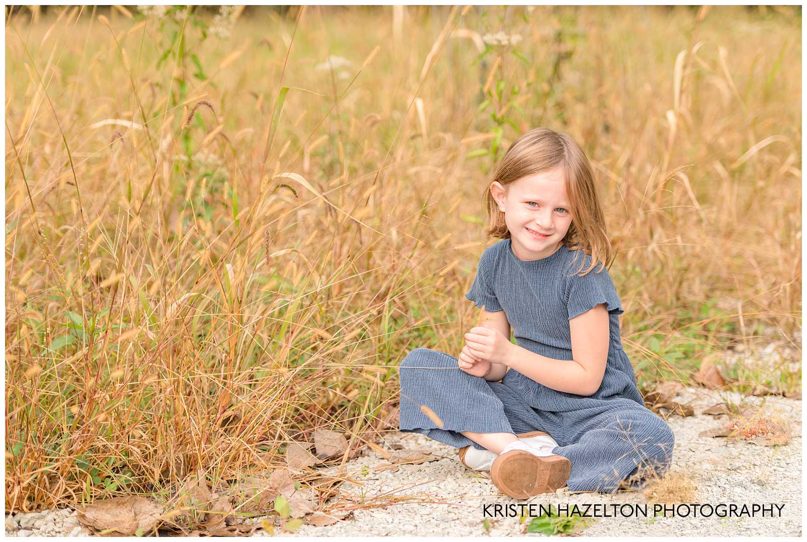 Girl in blue jumpsuit next to a field of cattails.