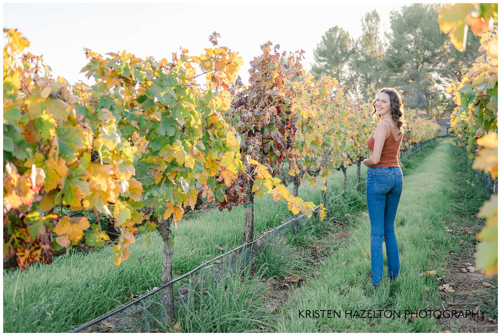 Girl in orange shirt and blue jeans walking through a vineyard