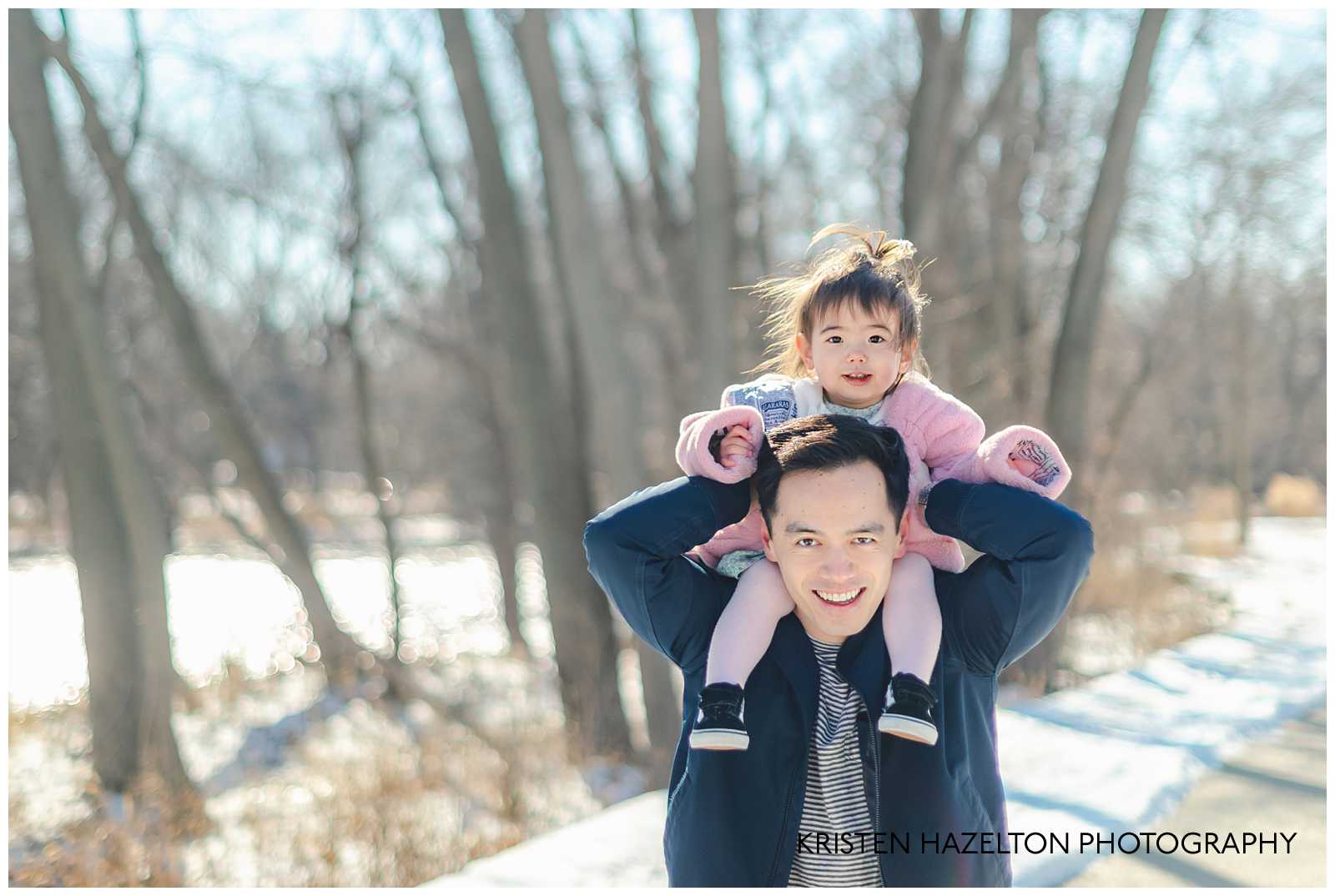 Dad bouncing toddler daughter on his shoulders at a Winter Family Photoshoot