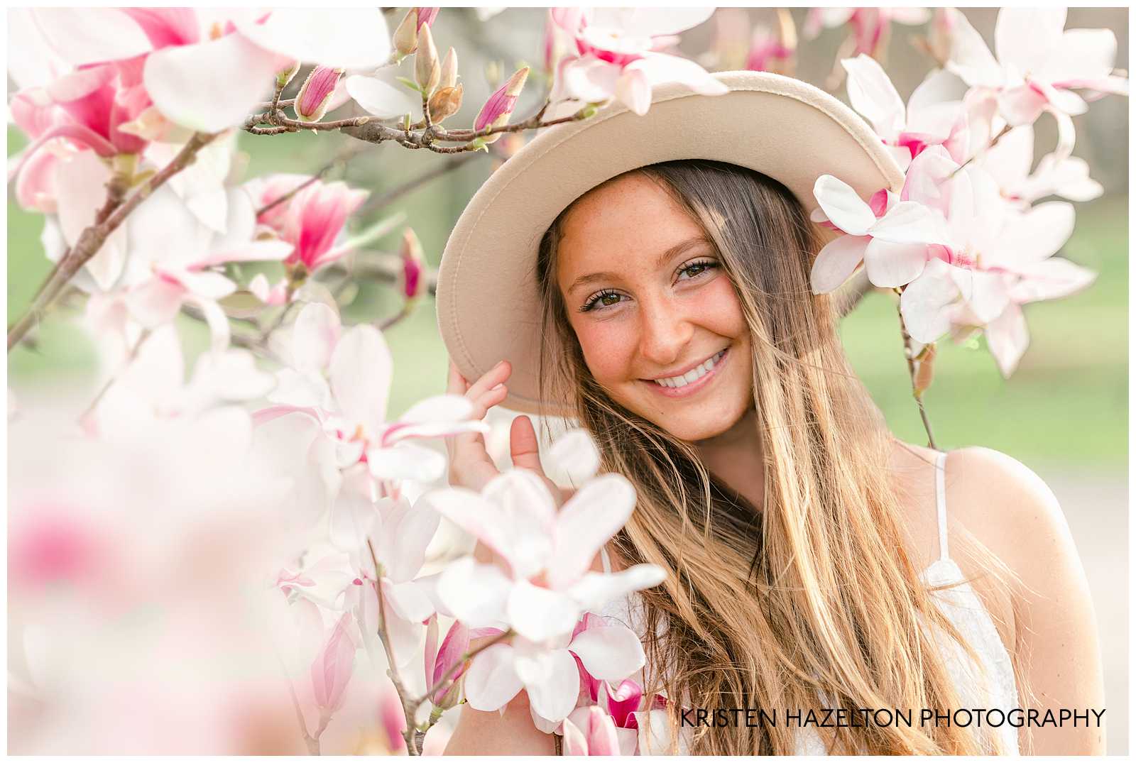 Senior girl with tan hat standing next to pink magnolias flowers for her elmhurst senior photos.