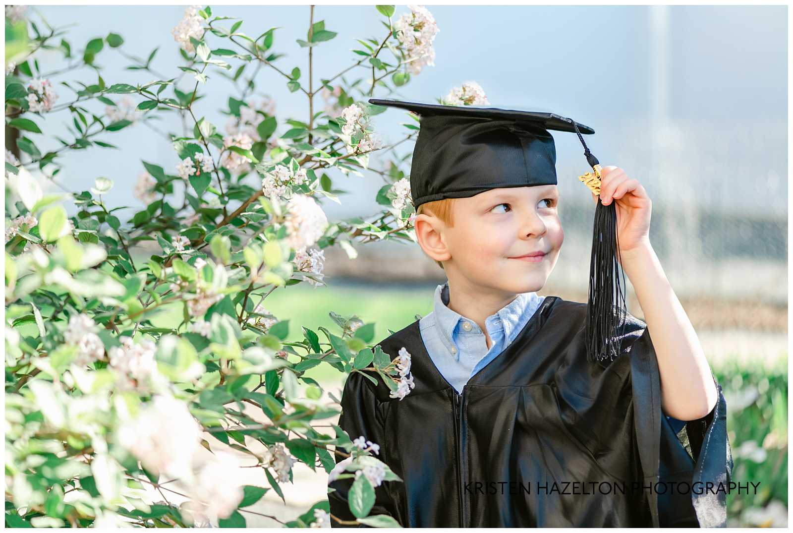 Kindergarten graduate wearing cap and gown and looking at his tassel.
