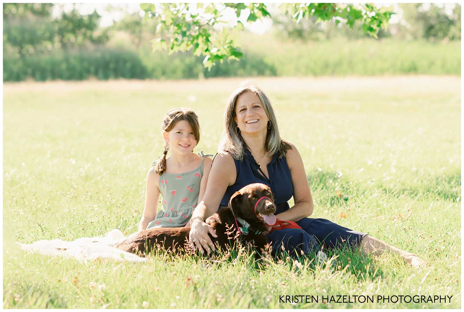 Mom and daughter petting their brown dog in a sunny meadow by Naperville Family Photographer Kristen Hazelton.