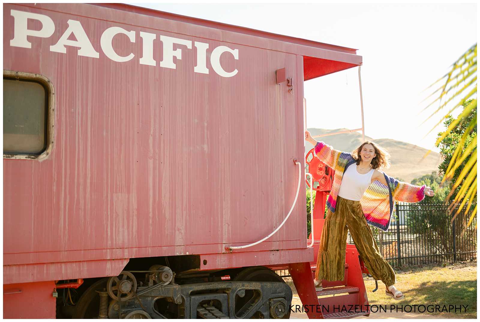 High school senior girl swinging on the back of a train caboose that reads "Pacific" at Niles in Fremont, CA