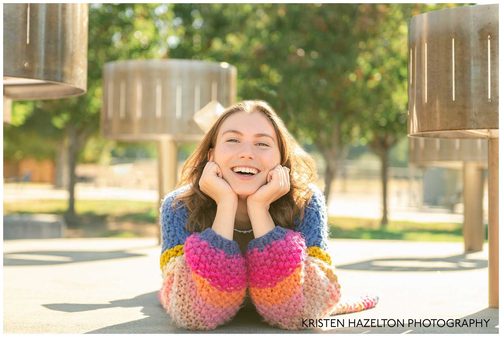 high school senior girl wearing a rainbow cardigan and lying down next to zoetrope sculptures in Niles in Fremont, California