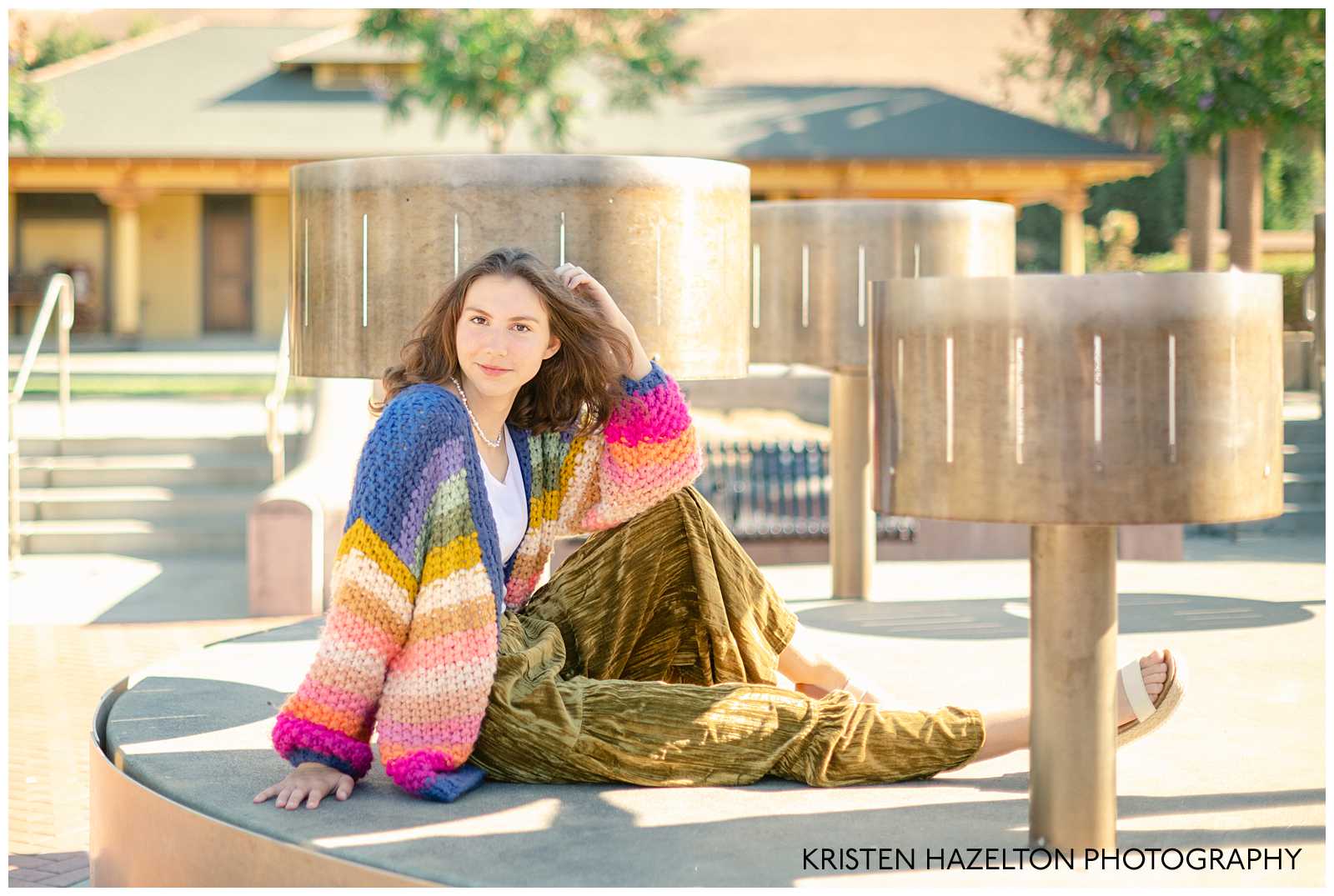 high school senior girl wearing a rainbow cardigan and seated next to zoetrope sculptures in Niles in Fremont, California