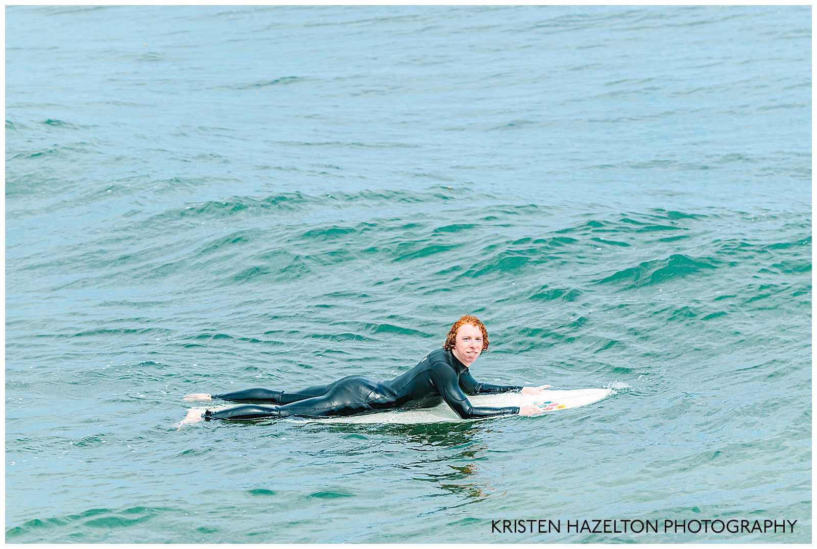 Portrait of a redheaded male surfer lying on his surfboard in the ocean. Surfing Photography by Kristen Hazelton.