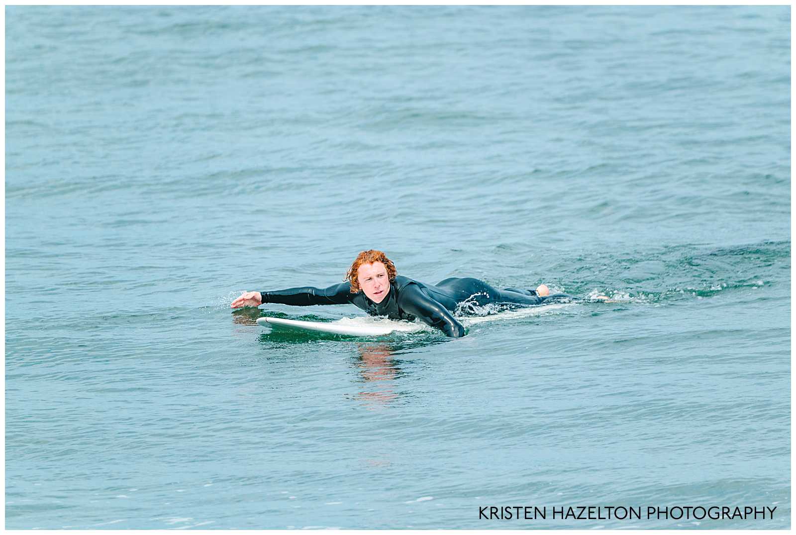 Redheaded man paddling to catch a wave while surfing. Surfing photography by Kristen Hazelton.