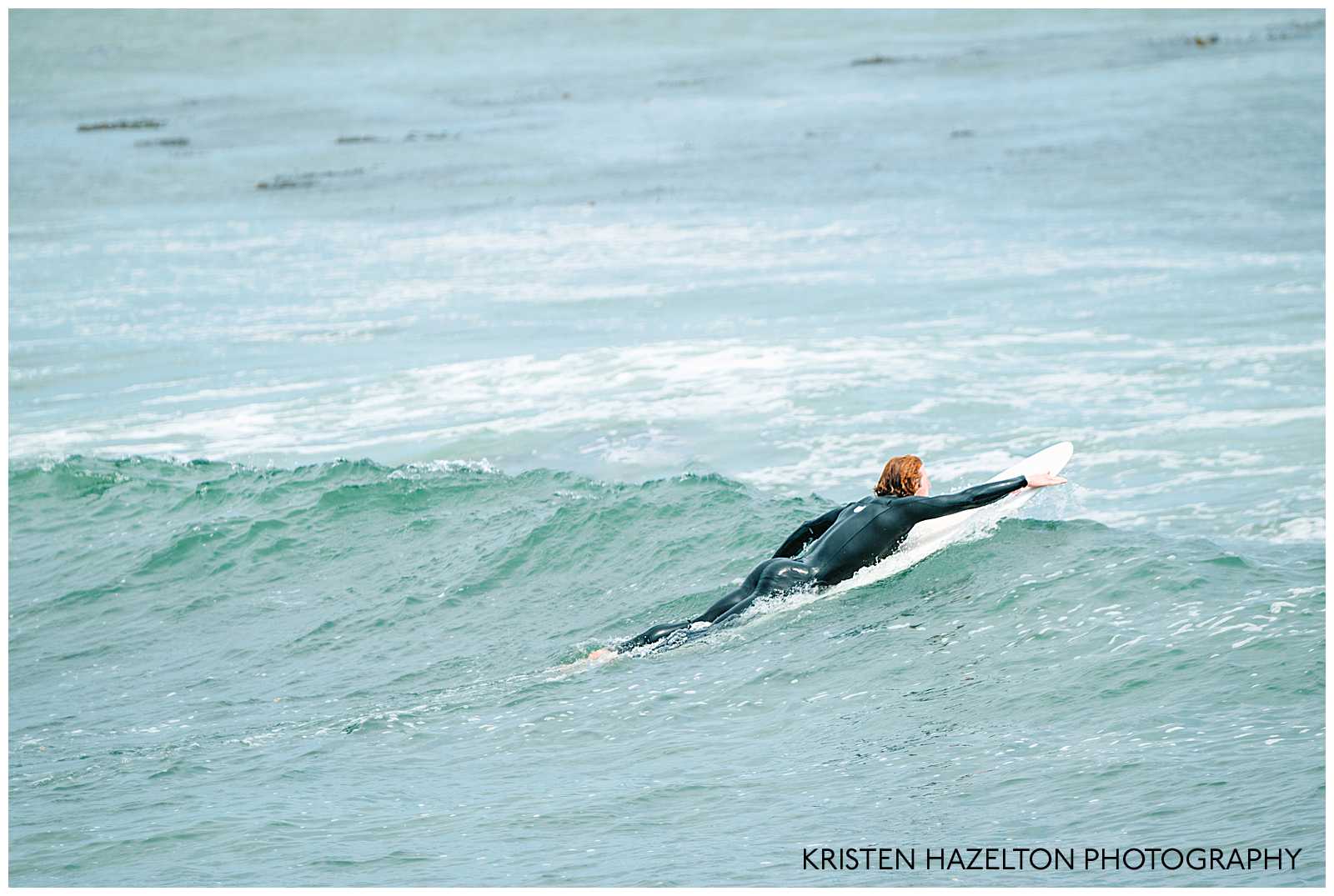 Redheaded surfer paddling over a wave at Pleasure Point in Santa Cruz, CA.