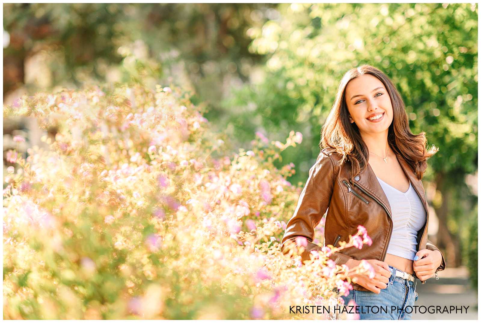 High school senior girl wearing a brown leather jacket and blue jeans with lots of purple flowers by Pleasanton CA senior photographer Kristen Hazelton